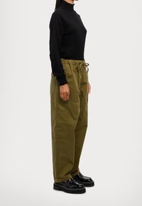 Czarny dopasowany sweter typu golf, w połączeniu z oliwkowymi spodniami cargo z elastycznym pasem i wieloma kieszeniami. Czarne buty na grubej podeszwie.