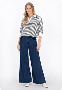 Pullover a righe bianche e blu navy con colletto, abbinato a jeans di denim scuri a gamba larga e sneakers bianche; vestibilità casual, tessuto testurizzato.