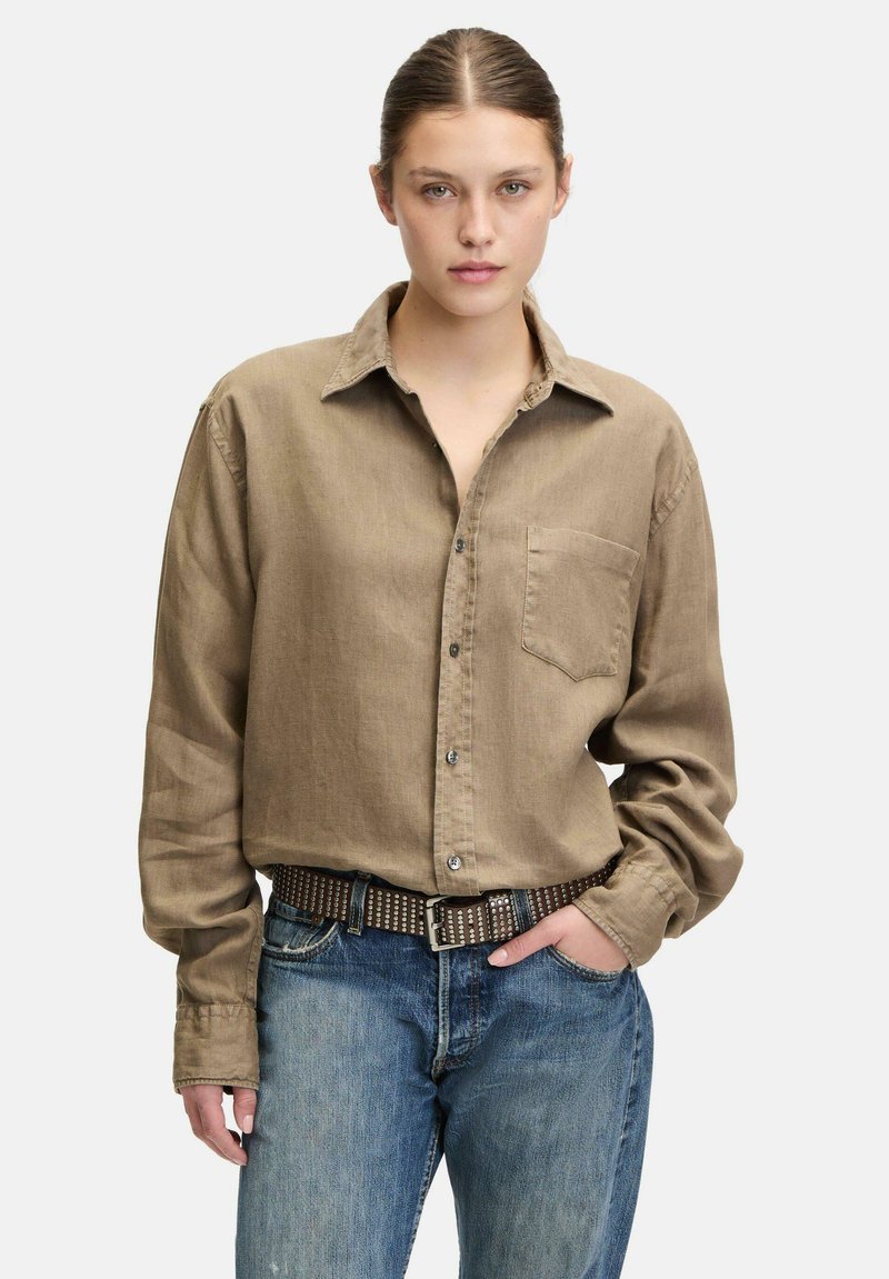 Hellbraunes, knöpfgemachtes Hemd mit einer Brusttasche, langen Ärmeln und lockerer Passform, kombiniert mit blauen Jeans und einem genoppten Gürtel.