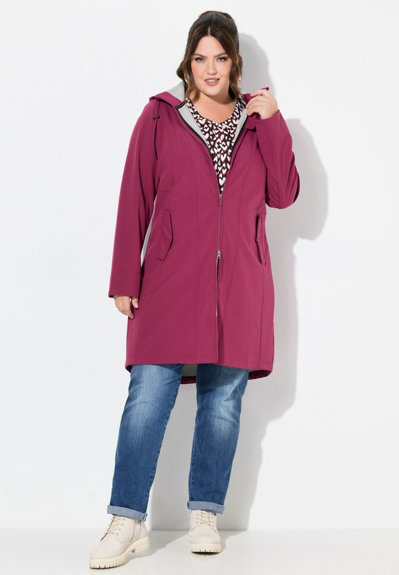 Fuchsia coat with zip closure, two front pockets, and a hood. Worn over a patterned top and paired with blue jeans and light-colored boots.