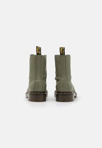 Bottines en cuir vert avec un bout arrondi, des coutures jaunes et des languettes noires. Semelles épaisses marron avec un léger talon.
