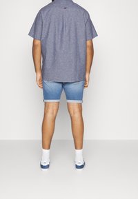 Camicia azzurra a maniche corte con bottoni, pantaloni corti di denim con orli arrotolati e scarpe da ginnastica bianche con accenti blu; texture liscia, vestibilità casual.