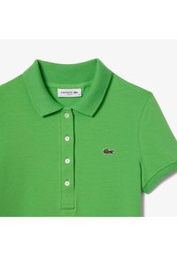 Groene Lacoste polo met een geribbelde kraag, een drie-knopenknopsluiting en een klein geborduurd logo op de linkerborst. Gladde structuur.
