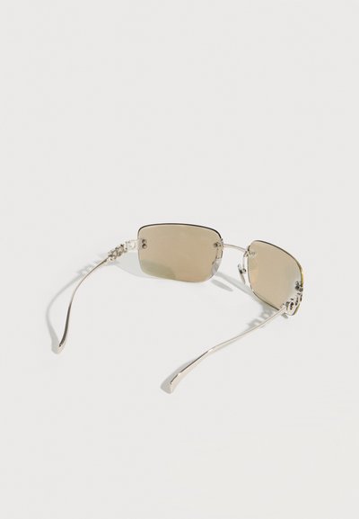Lunettes de soleil rectangulaires sans monture avec verres teintés brun clair et fines branches métalliques argentées sur fond blanc.