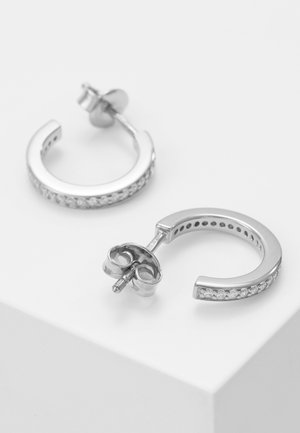 Paire de boucles d'oreilles demi-anneau en argent avec petites pierres transparentes le long du bord extérieur, présentées avec tige et fermoir papillon sur une surface blanche.