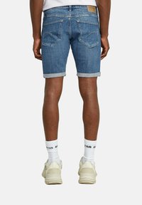 Shorts in denim leggeri di colore azzurro con risvolti, dotati di due tasche posteriori e di un'etichetta in pelle alla vita. Indossati con calzini bianchi e sneakers.