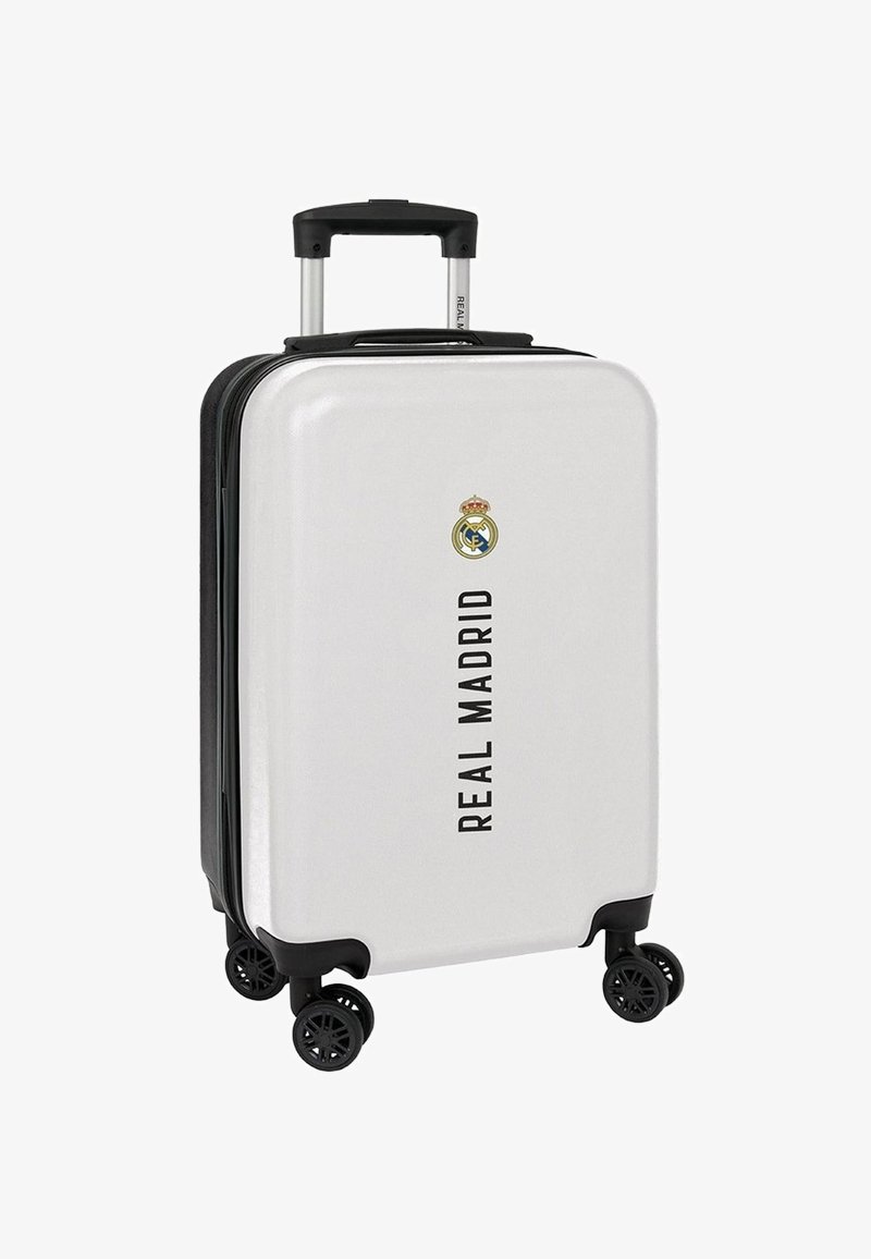 Valise rigide blanche avec des accents noirs ; elle dispose d'une poignée télescopique, de quatre roues et d'un texte noir indiquant "REAL MADRID" avec un logo.