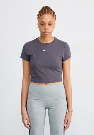 Siva skraćena majica s kratkim rukavima s bijelim Nike logom. Uparena s visokim sivoj tajicama. Jednostavna pozadina.
