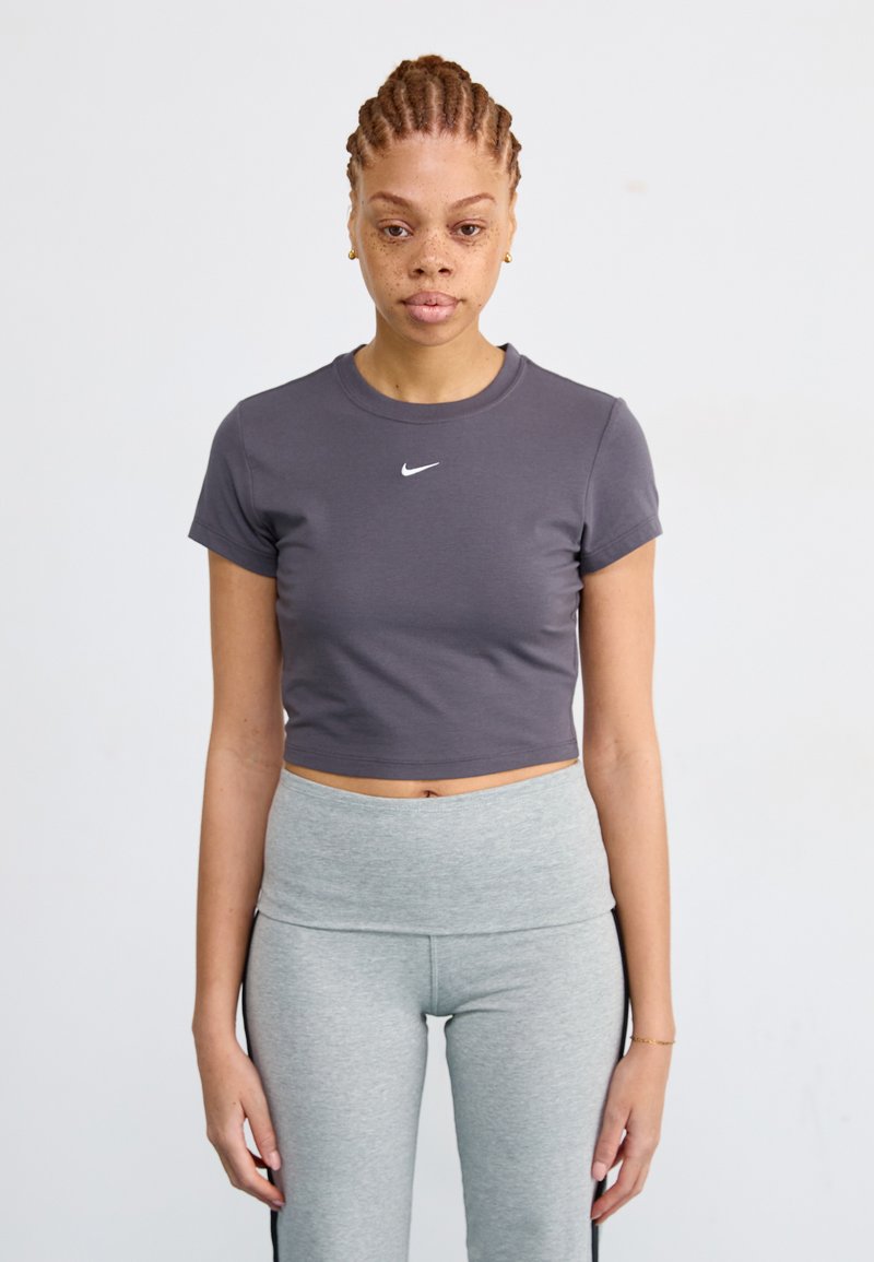Grijs cropped t-shirt met korte mouwen met een wit Nike-logo. Gecombineerd met hoog-getailleerde grijze leggings. Eenvoudige achtergrond.