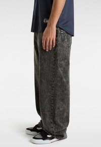 Vaqueros de mezclilla lavada en negro con un corte holgado, con textura descolorida y bolsillos laterales. Combinados con zapatillas negras y blancas.