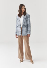 Blazer de tweed de doble botonadura en azul y blanco, con grandes botones, combinado con pantalones anchos beige y zapatos planos beige puntiagudos.