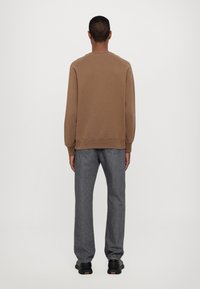 Bruine sweatshirt met een geribbelde kraag en manchetten, gecombineerd met loszittende grijze jeans en zwarte sneakers, bekeken vanaf de achterkant.