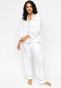 Witte pyjama-set met zwarte biezen, bestaande uit een langslijfs knoopjes blouse en losse broek, gemaakt van zachte stof.