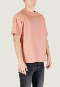 Camiseta rosa de algodón con mangas cortas, cuello redondo y un pequeño logo blanco de Calvin Klein Jeans en el frente. Se lleva con unos vaqueros de mezclilla negros.