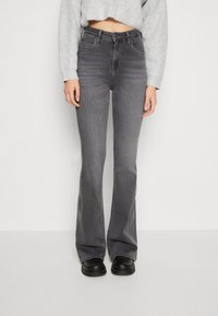 Vaqueros grises acampanados de cintura alta, confeccionados en denim. Presentan bolsillos frontales y costuras visibles a lo largo de las costuras. Combinados con un suéter corto de color gris claro.