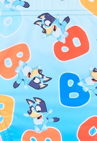 Tessuto per costumi da bagno con uno sfondo azzurro chiaro e cani dei cartoni animati stampati in varie pose, con lettere colorate "B" in arancione e blu.
