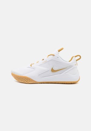 Chaussure de sport Nike blanche et dorée avec semelle en gomme, logo Swoosh latéral, col rembourré, et languettes de tirage sur la languette et le talon.
