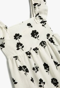 Sort kjole med blomsterprint og volanger, lavet af struktureret hvidt stof, med et tætsiddende liv og en flagrende nederdel.