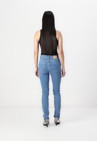 Jeans ajustados de color azul con cintura de media altura, diseño de cinco bolsillos y una etiqueta marrón en la parte posterior de la cintura, combinados con tacones altos plateados.