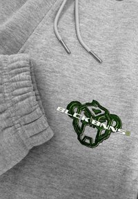 Grijze hoodie van een gestructureerde stof, met een groene geborduurde aap logo en de tekst "BLCKBNNS" in het wit over de borst.