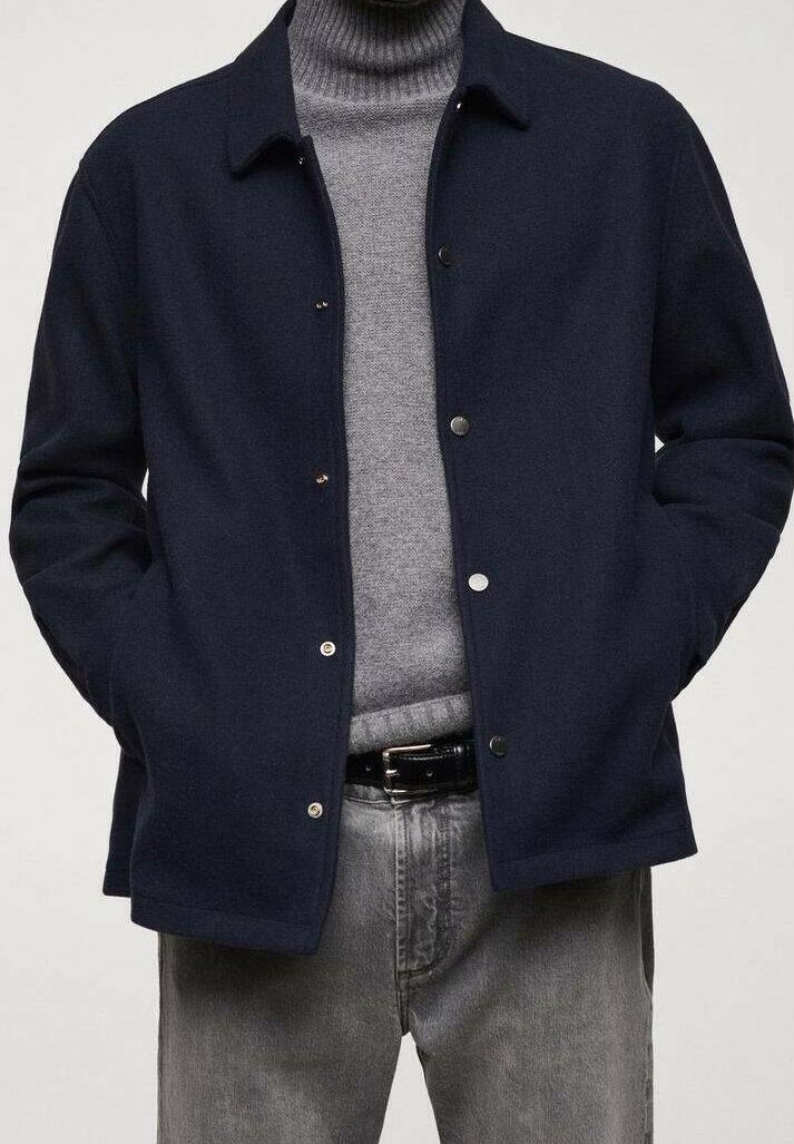 Navy blue wool jacket with snap buttons, classic collar, worn over a gray knitted turtleneck, paired with gray jeans and a black belt.
