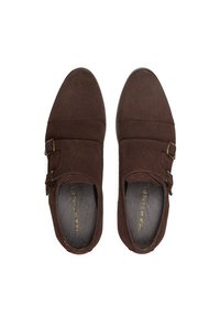 Zapatos de ante marrón tipo slip-on con dos hebillas laterales, puntera redonda y un interior suave. Suela plana con un patrón de relieve mínimo.