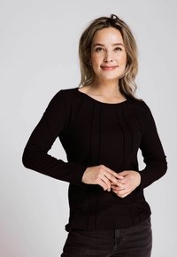 Schwarzes, geripptes Langarmoberteil mit dezenten vertikalen Nahtdetails, rundem Halsausschnitt und texturiertem Stoff, kombiniert mit dunklen Jeans.