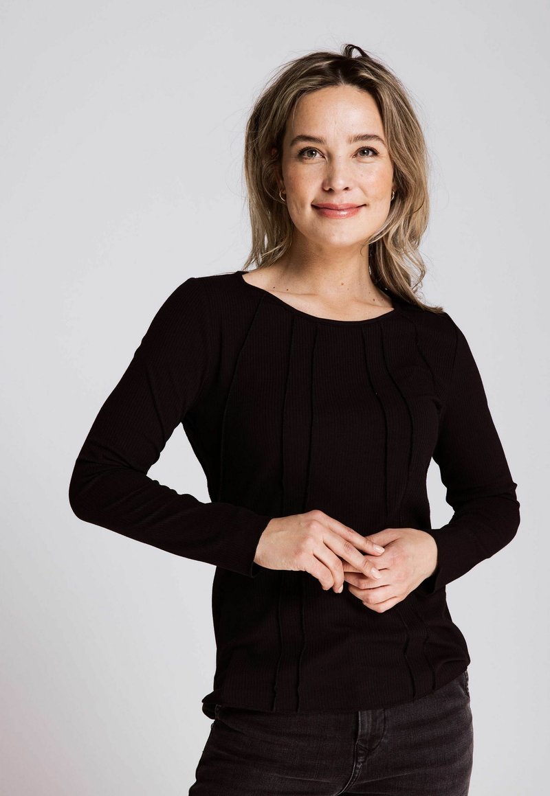 Schwarzes, geripptes Langarmoberteil mit dezenten vertikalen Nahtdetails, rundem Halsausschnitt und texturiertem Stoff, kombiniert mit dunklen Jeans.