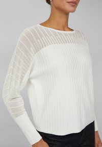 Pull blanc côtelé avec une partie supérieure texturée et transparente et une partie inférieure unie. Comprend des manches longues et un col rond. Coupe standard.