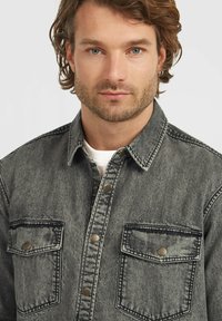 Gray denim shirt featuring a button-up front, two chest pockets with button closures, and contrasting black stitching.