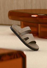 Μπεζ σανδάλια με λουράκια, κατασκευασμένα από μαλακό σουέτ με δύο πλατιά λουράκια, διαθέτουν μαύρη λαστιχένια σόλα και μικρό λογότυπο ως διακοσμητικό.