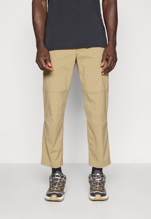 Beige Cargo-Hosen aus leichtem, strukturiertem Stoff, mit mehreren Taschen und geradem Schnitt. Kombiniert mit dunkelgrauen Sportschuhen.