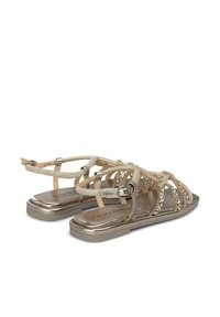 Sandalias metálicas doradas con correas ajustables en el tobillo, cristales decorativos y una suela plana con detalles texturizados.