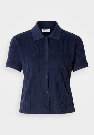 Tamnoplava polo majica s kratkim rukavima i ovratnikom, s teksturiranim uzorkom u obliku dijamanta i zatvaračem na dugmad.