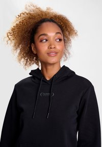 Svart hoodie tillverkad av bomullsblandning, med en framficka och snörning i huvan. Inkluderar en subtil logotyp på bröstområdet.