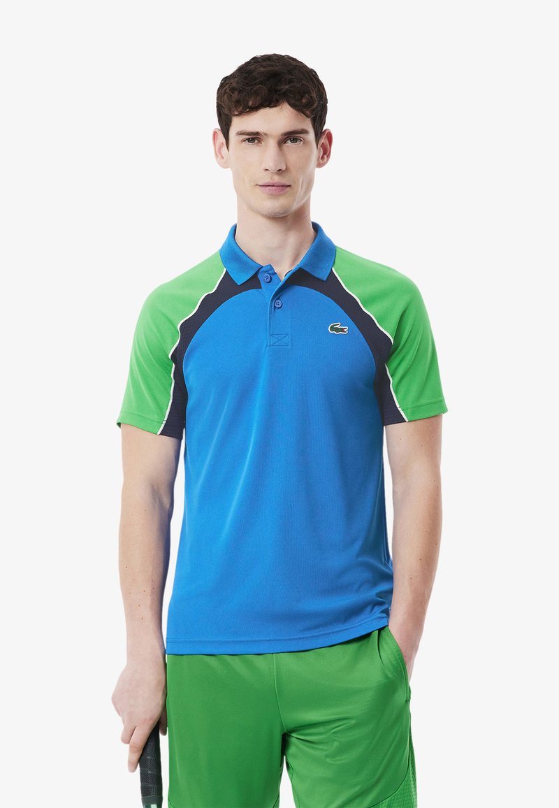 Blå och grön polo skjorta med korta ärmar, med krage, marinblå detaljer och en liten logotyp på bröstet. Mjuk, atletisk tyg.