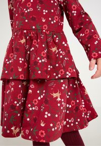 Czerwona sukienka w kwiaty z długimi rękawami, z warstwowym krojem spódnicy. Wzór zawiera kwiaty, ptaki i jelenie, wykonana jest z miękkiego materiału bawełnianego.