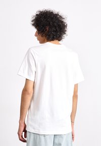 Λευκό βαμβακερό t-shirt με κοντά μανίκια, στρογγυλή λαιμόκοψη και χαλαρή εφαρμογή· εμφανίζεται από πίσω, δείχνοντας απλότητα και λεία υφή.