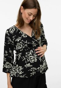 Top portefeuille floral noir avec des manches 3/4, présentant des motifs de fleurs blanches. Il se resserre à la taille, offrant un ajustement confortable. Texture de tissu douce.