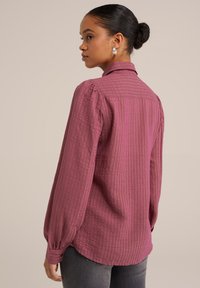 Camicia a maniche lunghe con texture di un profondo colore rosa, con colletto e polsini abbottonati, caratterizzata da un sottile motivo a reticolo.