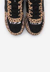 Las zapatillas de deporte con estampado de leopardo presentan una combinación de piel de vaca marrón y tela negra, con cordones negros y una suela de goma texturizada para mayor agarre.