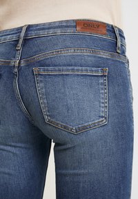 Jeans de denim azul oscuro con una textura suave, que cuentan con una etiqueta de cuero etiquetada como "ONLY" y bolsillos traseros estándar con detalles de costura sutiles.