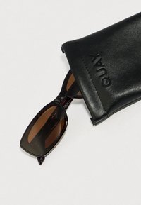 Čierne kožené puzdro s vyrazeným logom "QUAY" obsahuje tmavohnedé slnečné okuliare s obdĺžnikovým rámom a tónovanými sklami.