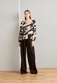 Blusa fluida a maniche lunghe in stampa astratta beige e nera, con scollatura a V e dettagli con bottoni, abbinata a pantaloni neri a gamba larga.