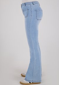 Lichtblauwe denim flared jeans met een hoge taille, vijf zakken, contrasterende stiksels en een gladde textuur, gecombineerd met grijze sneakers.