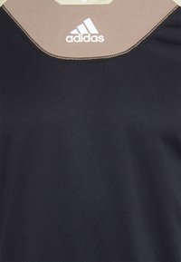 Top atlético negro con un cuello beige, confeccionado con una tela suave y elástica, y con un logotipo blanco de Adidas en la parte frontal.