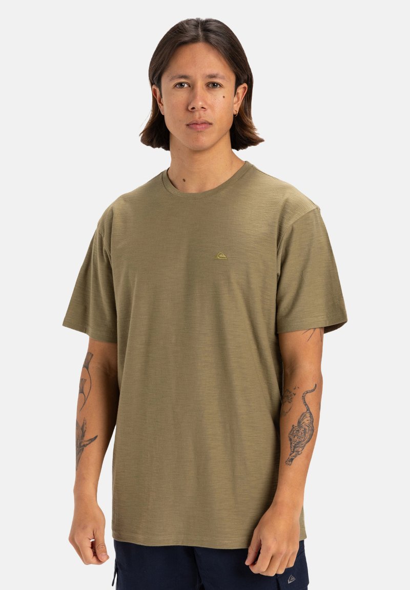 Camiseta de manga corta en verde oliva con escote redondo y tejido texturizado. Presenta un pequeño detalle de logo en el pecho.