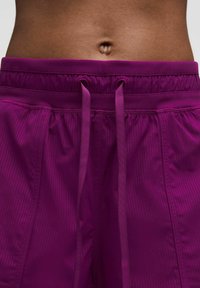 Pantalones cortos deportivos morados con una textura acanalada, cinturilla elástica y cordones. Presentan una tela suave para mayor comodidad y ajuste.