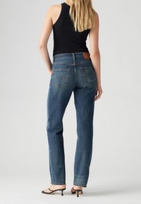 Džíny s vysokým pasem v modré denimové barvě, rovného střihu, s kapsami na zadní straně a koženou nášivkou. Kombinované s černým tílkem a sandály.