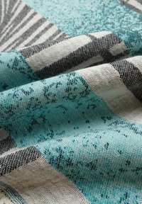 Textiel met een turquoise en witte patroonstof met zwarte accenten. Het materiaal heeft een gestructureerde afwerking en variërende geometrische ontwerpen.